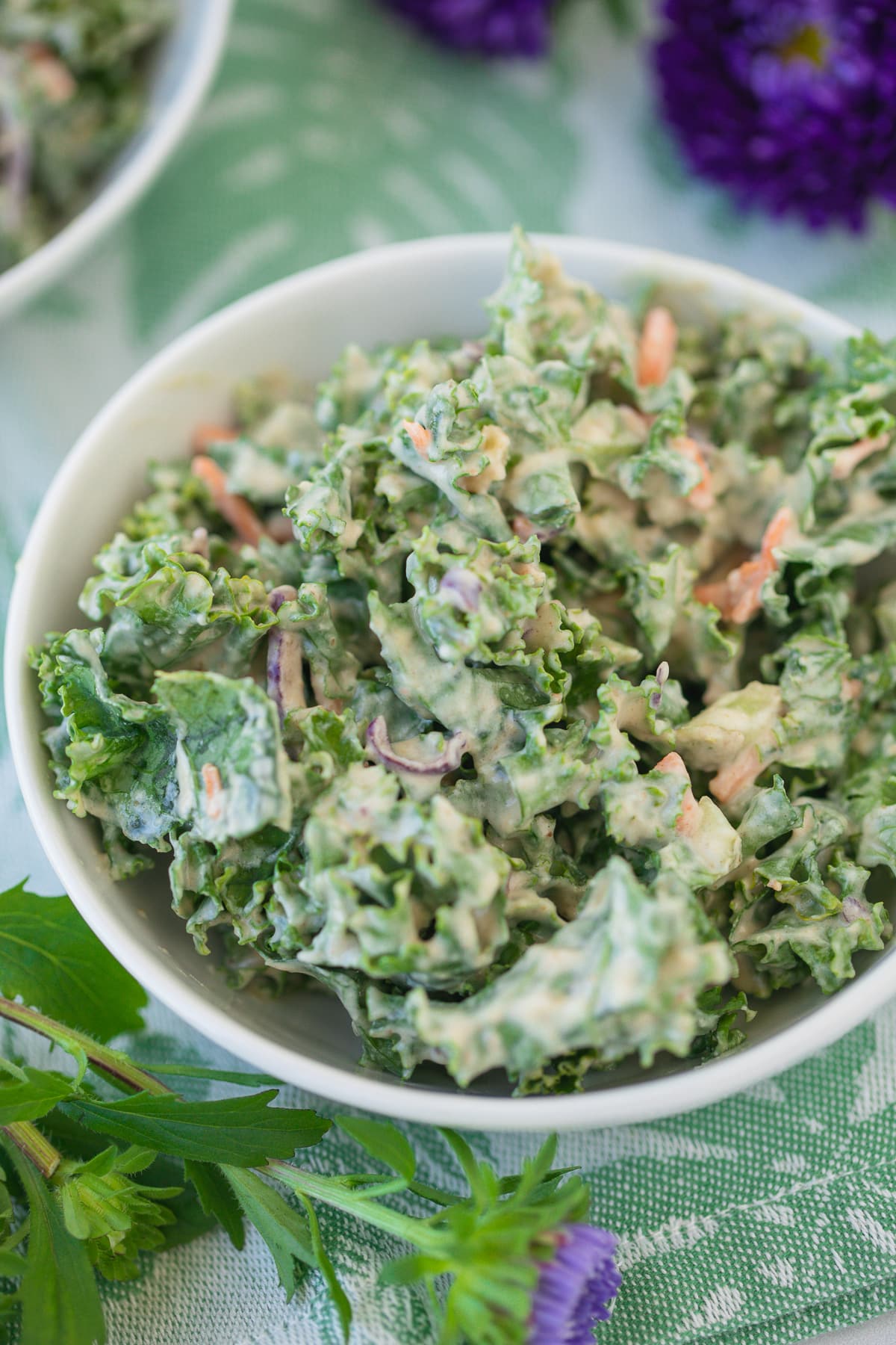 bowl of kale salad with purple flowers on a table.