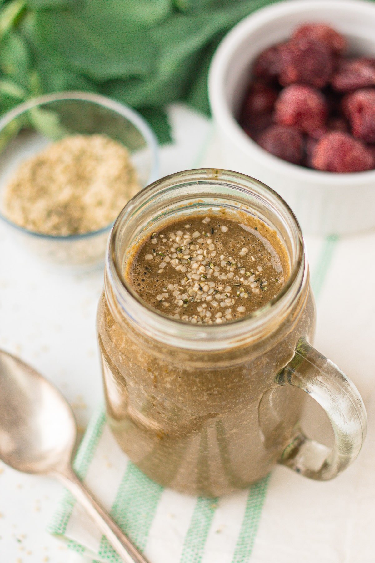 greens smoothie with cherries, hemp seeds, and collard greens in the background