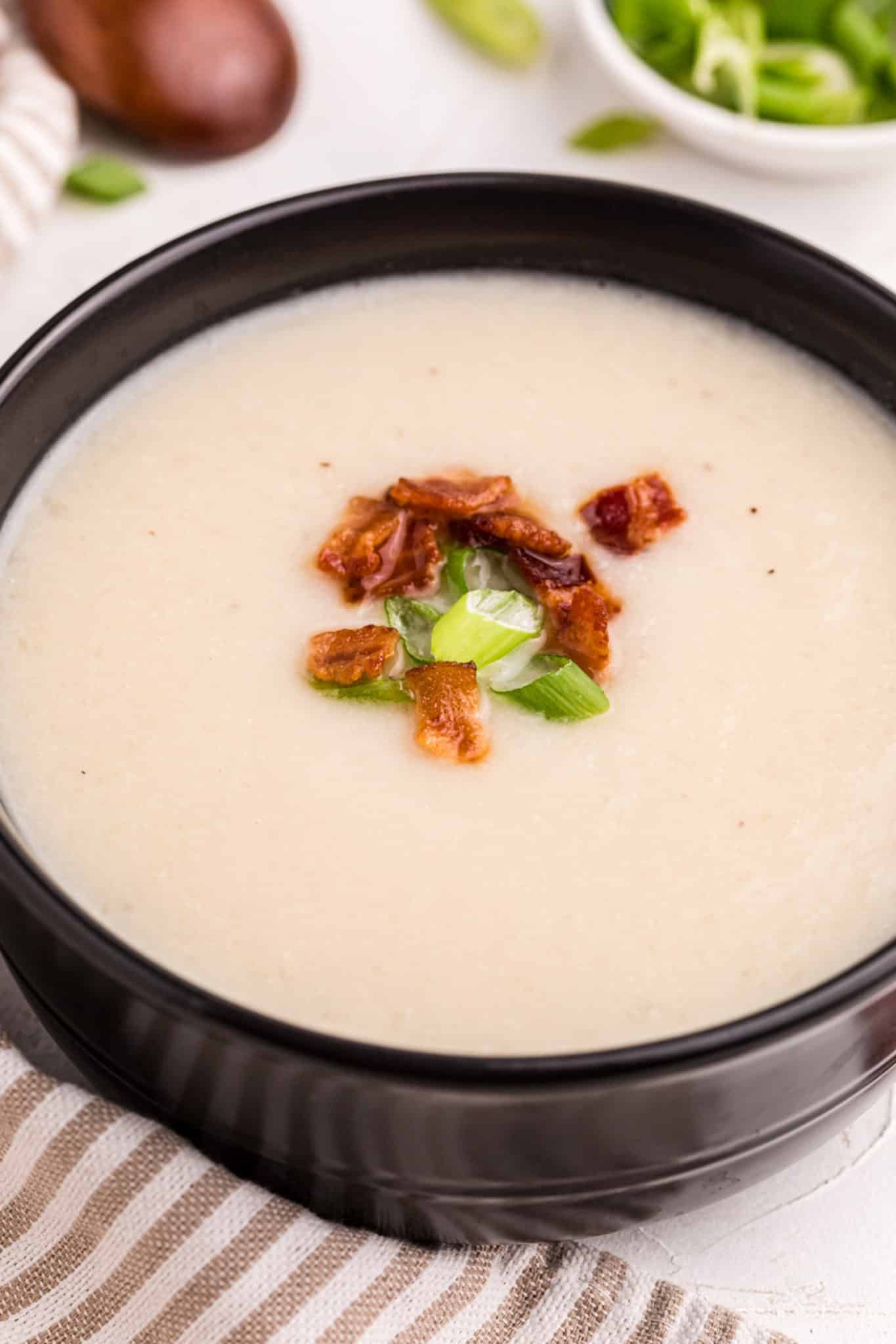 creamy cauliflower soup served in a black bowl.