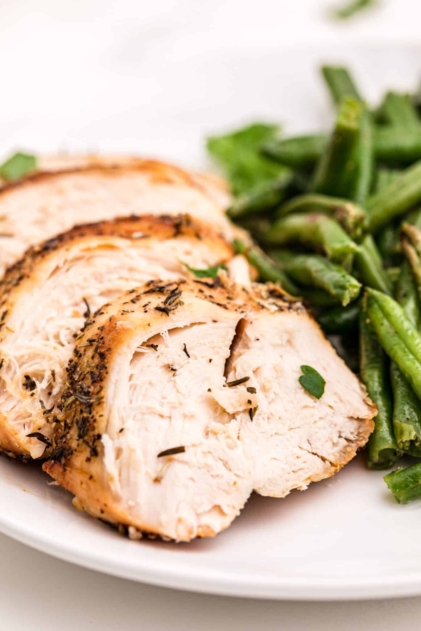 sliced air fryer turkey tenderloin on plate with green beans.