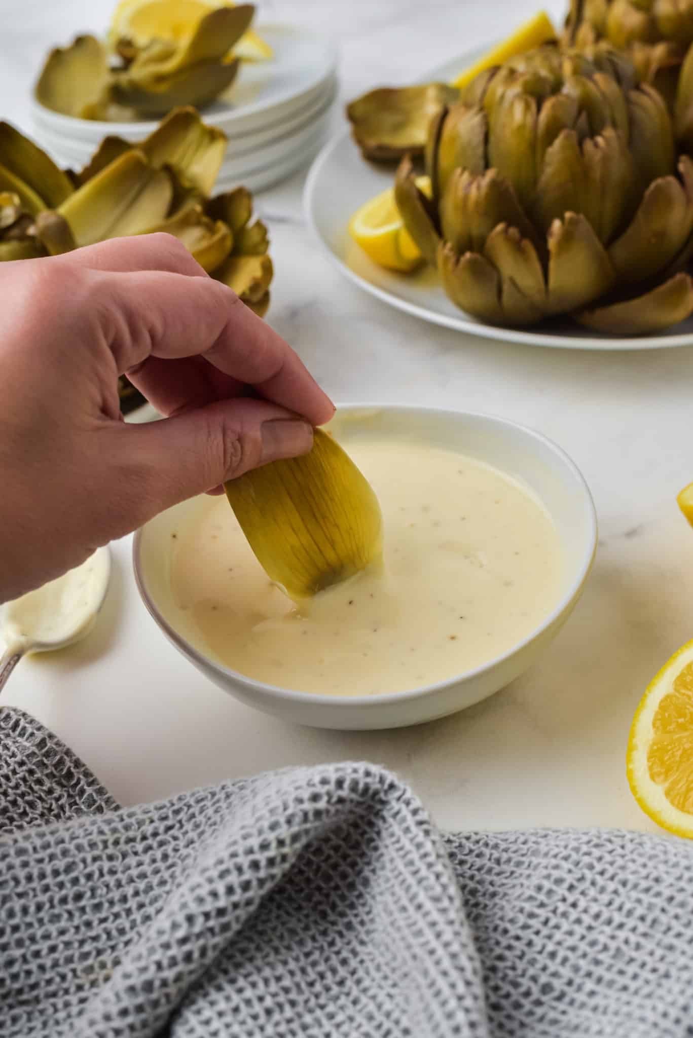 hand dipping an artichoke leaf into the dip.