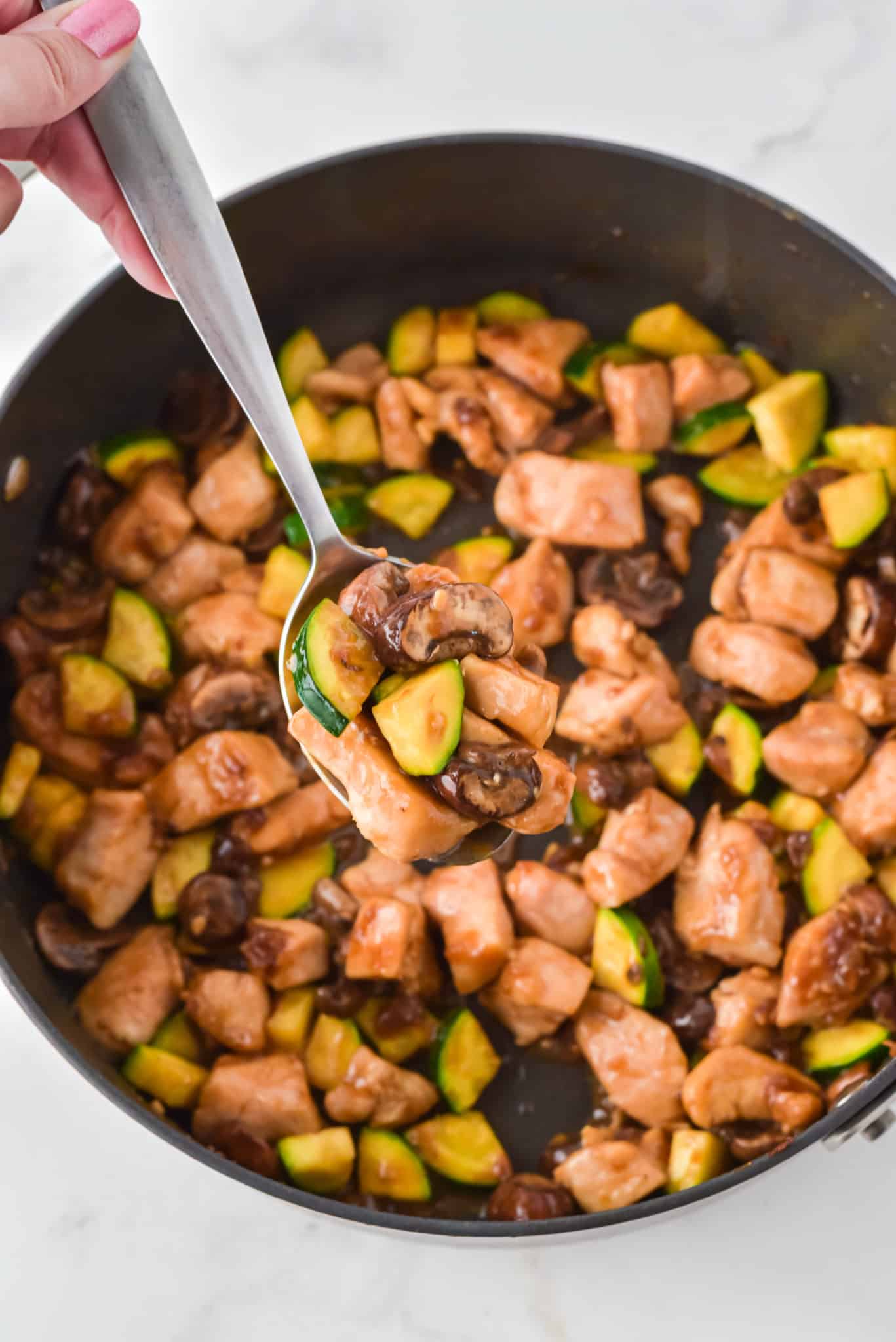 A serving spoon of Panda Express copycat mushroom chicken over a skillet.