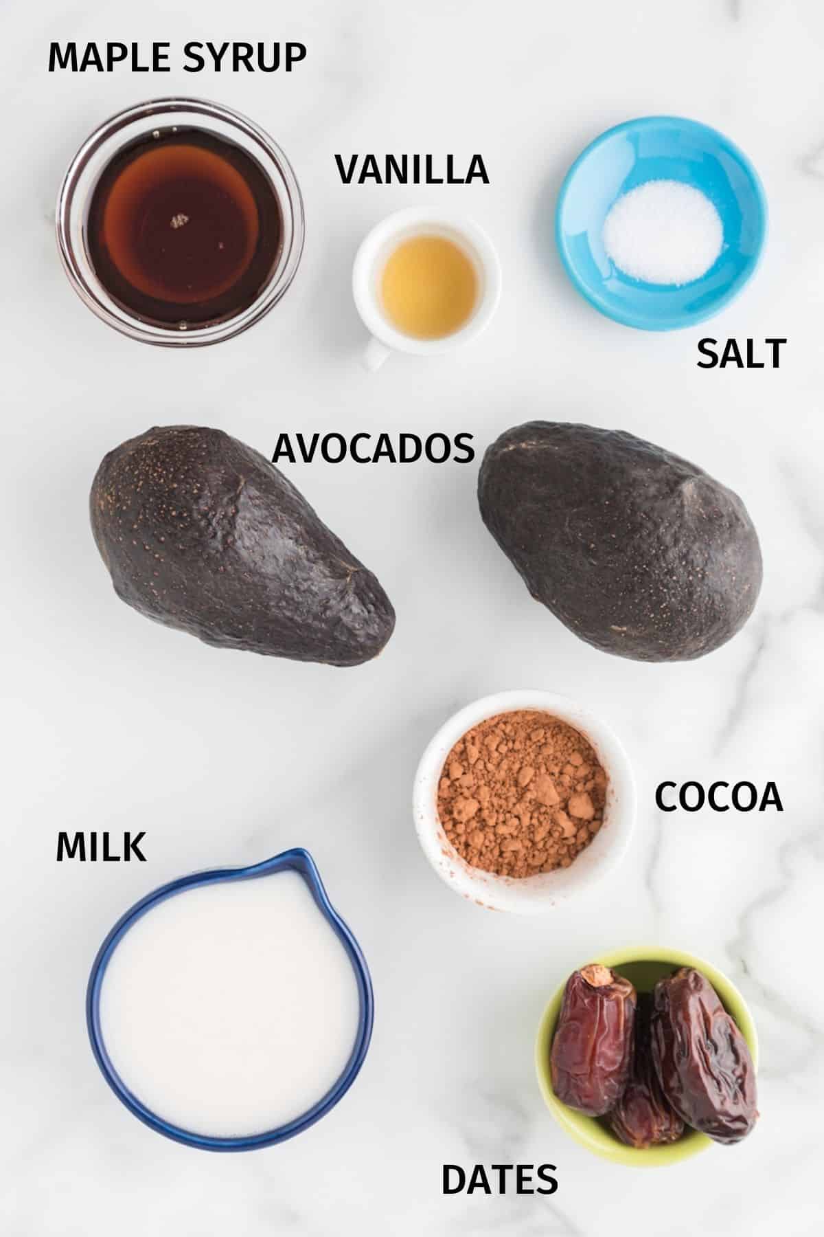 Ingredients for chocolate avocado pudding on a white surface.