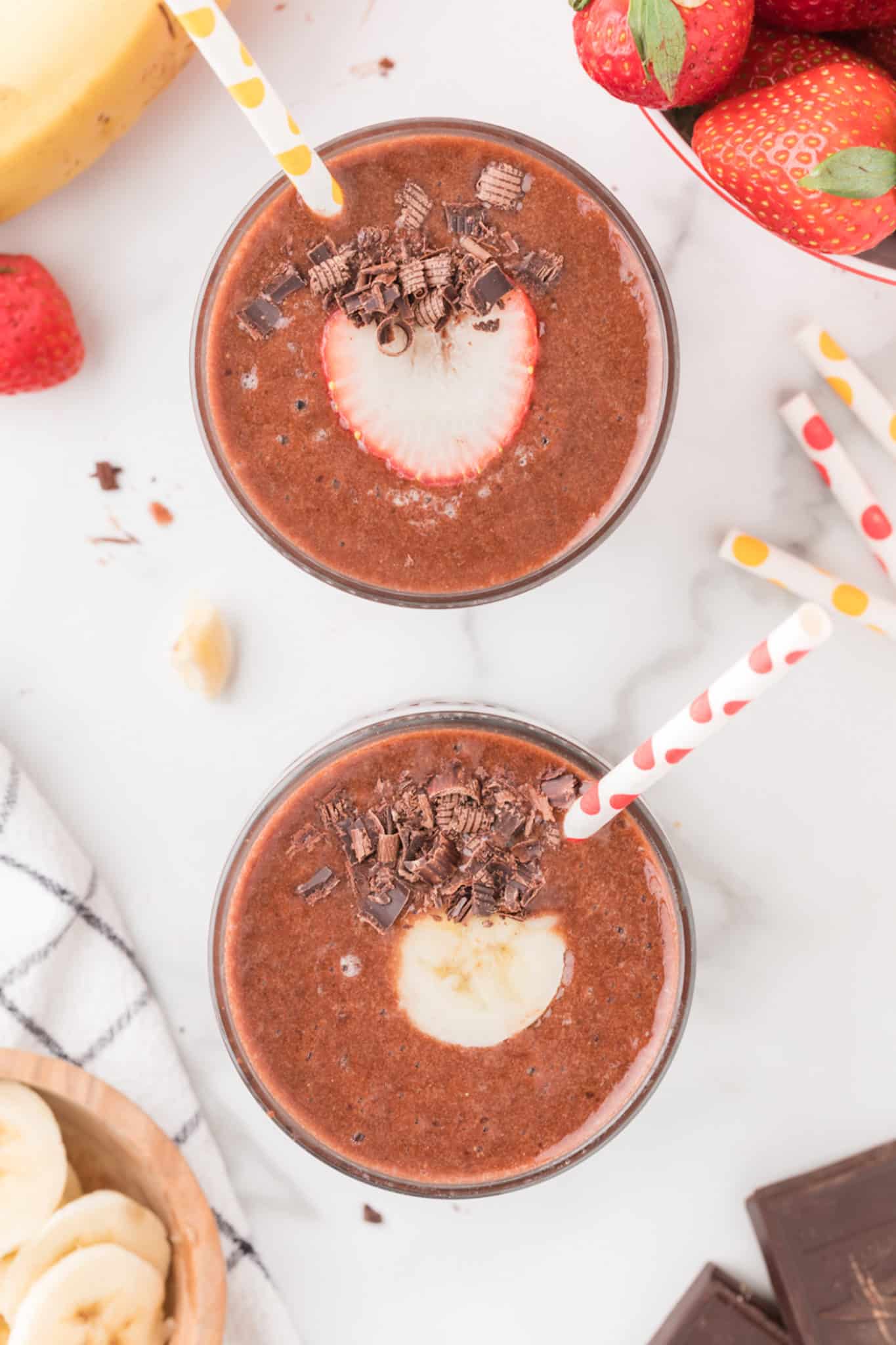 two glasses of chocolate strawberry banana smoothie with straws.