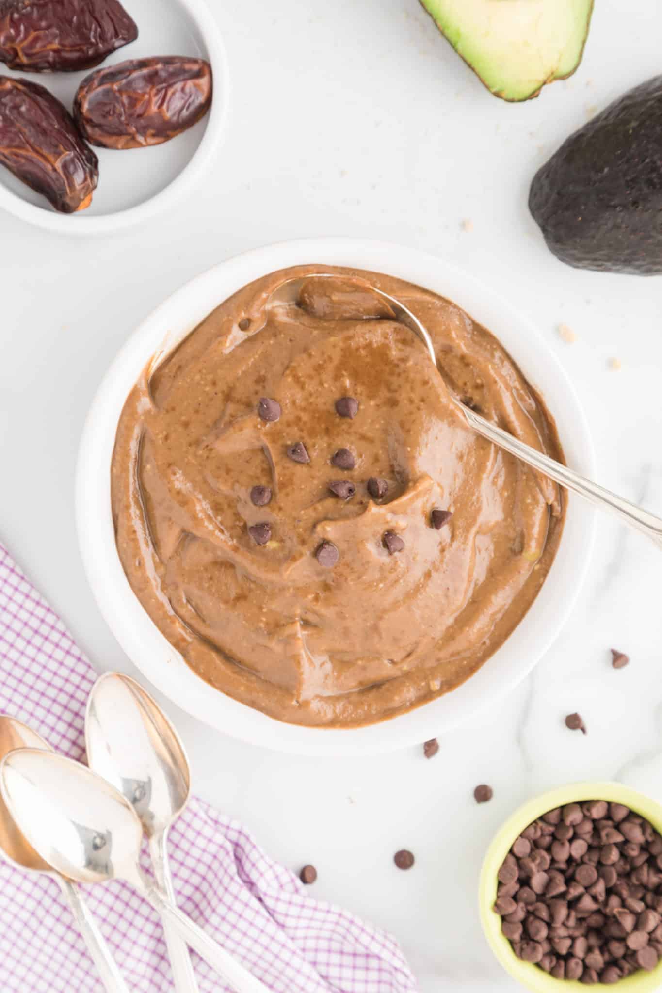 Top view of a white bowl with spoon and chocolate avocado pudding topped with chocolate chips.