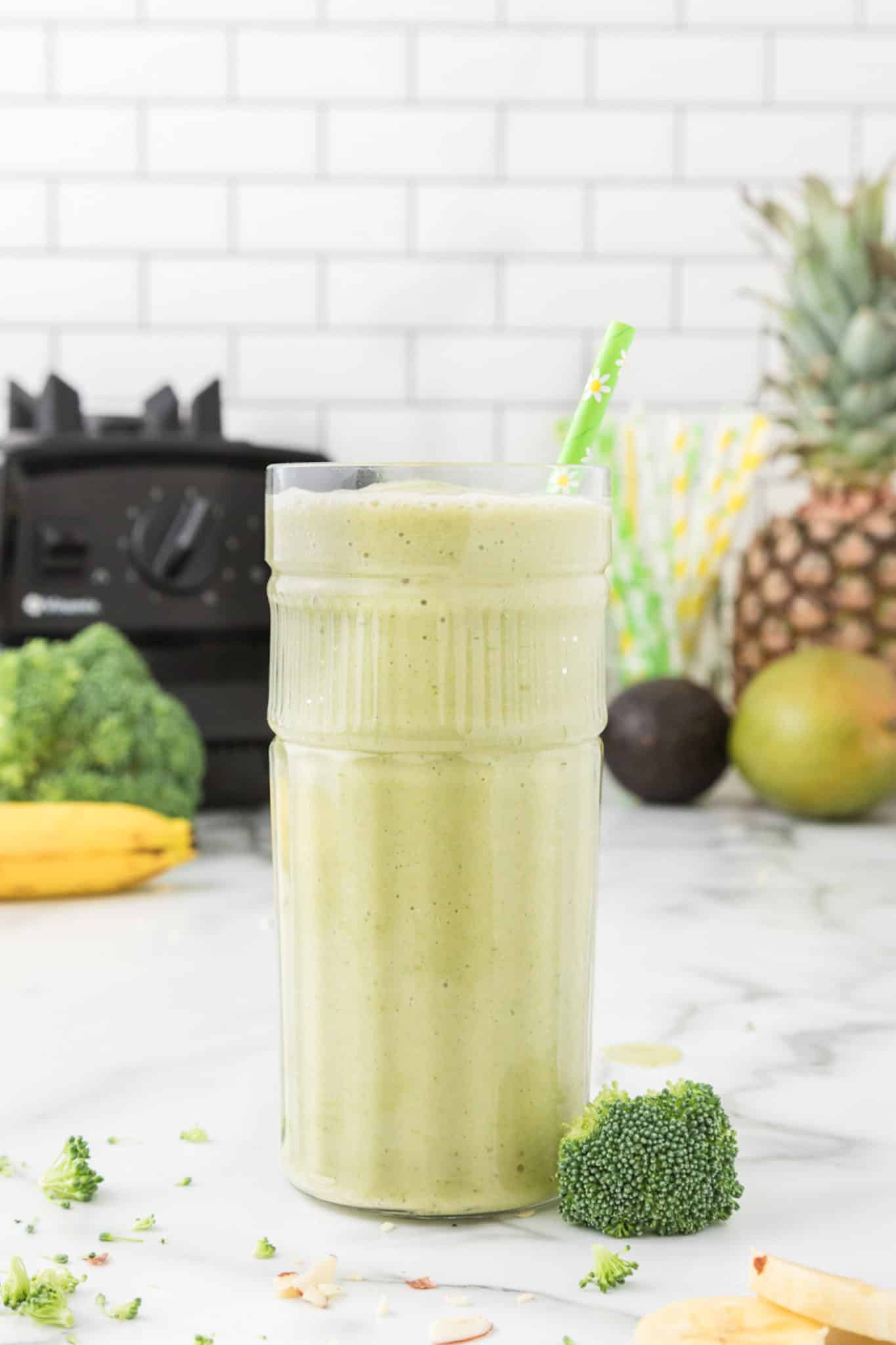 glass of green broccoli smoothie with a straw on the countertop.