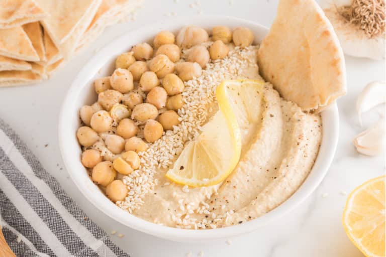 A white bowl of oil-free hummus topped with chickpeas and sesame seeds.