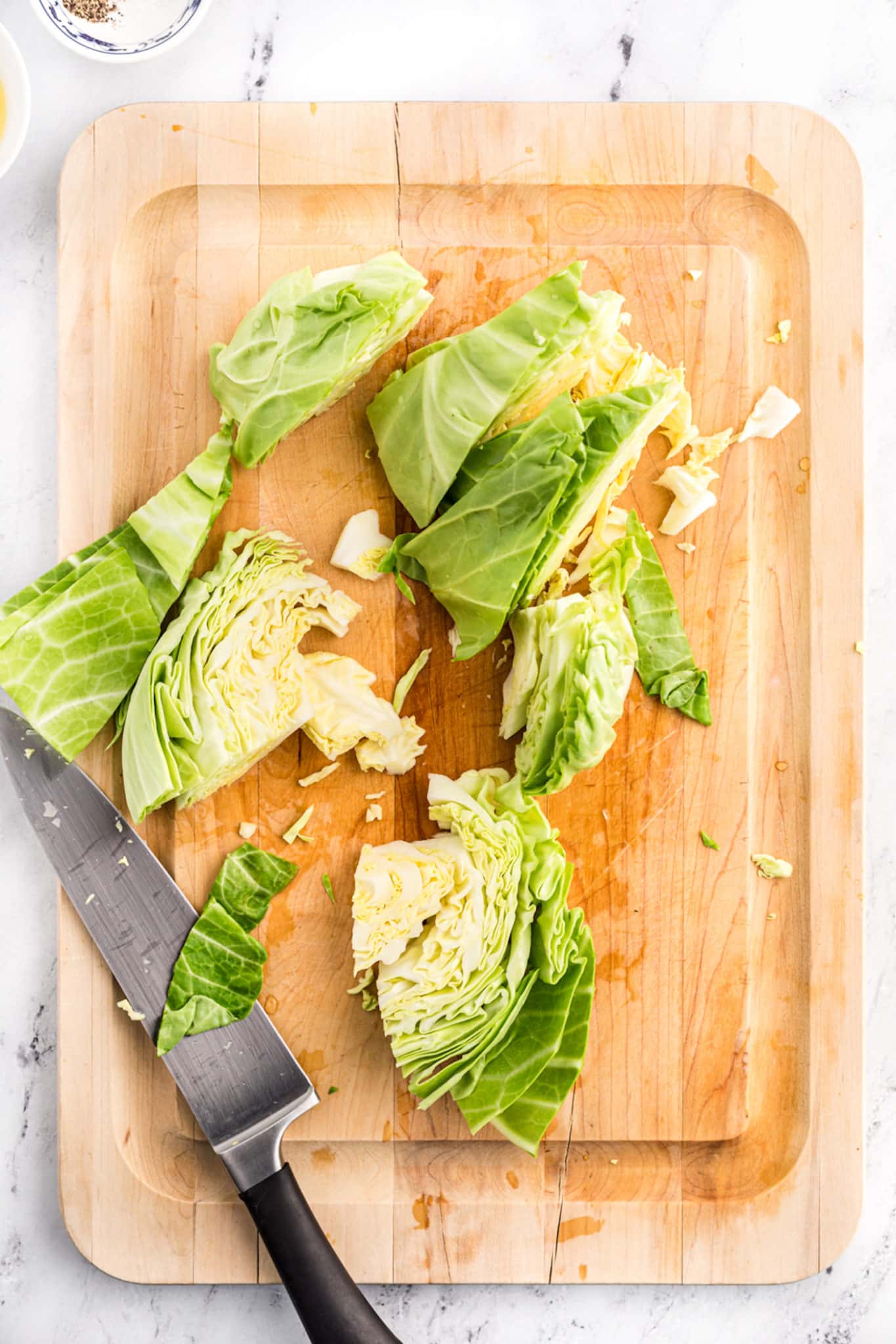 A chef's knife and a cut cabbage head on a wood cutting board.