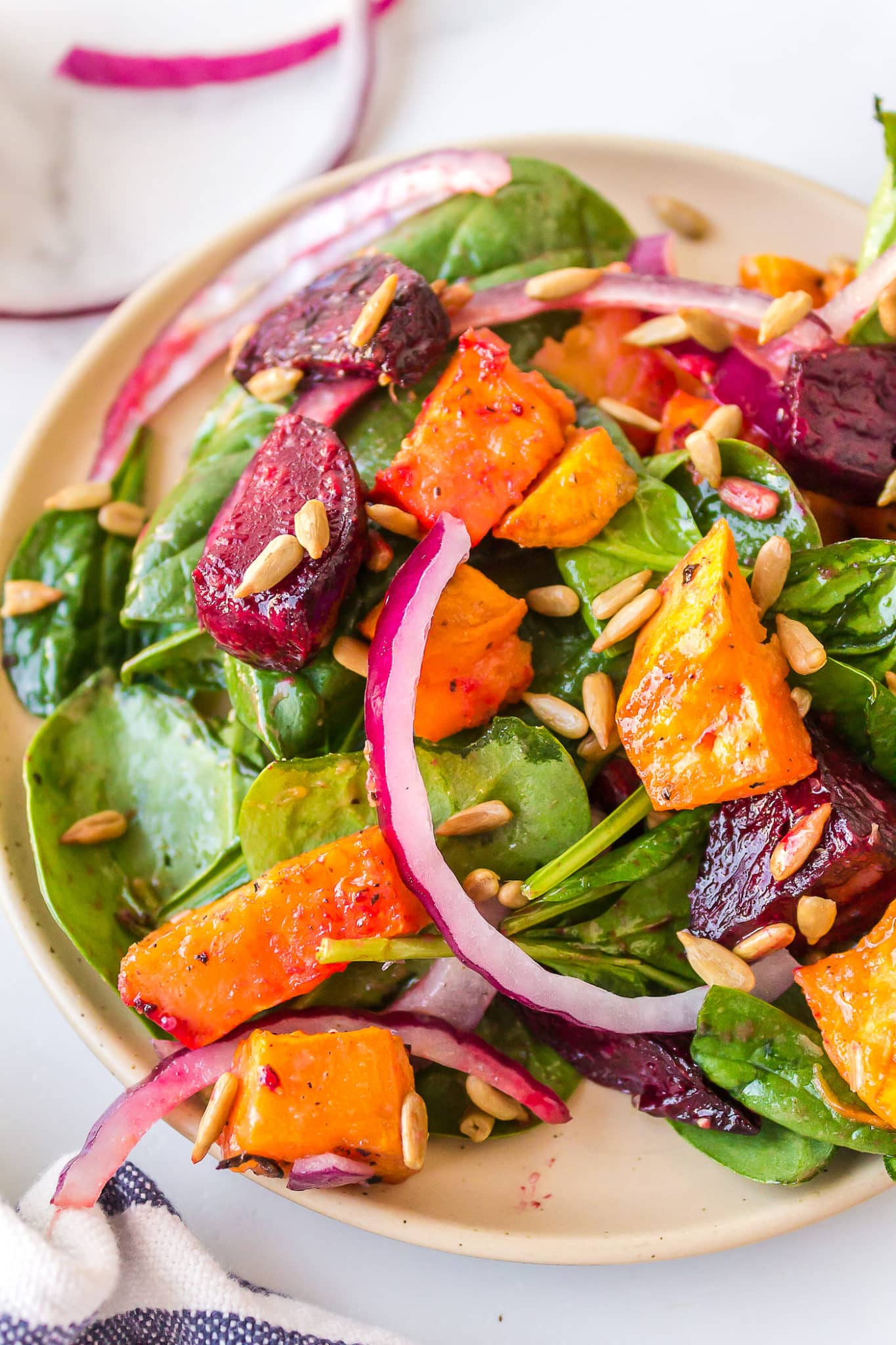 Close up of diced beets and sweet potatoes on a dressed spinach salad.