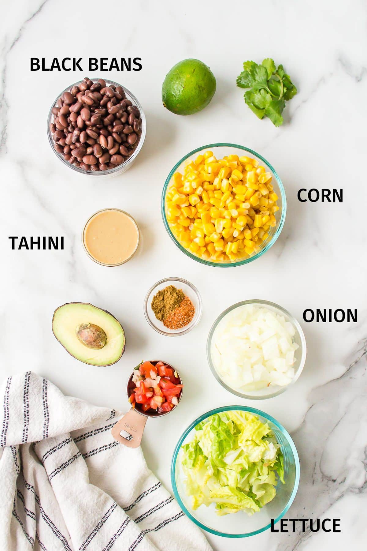 Ingredients for a Mexican Buddha bowl in small bowls on a white surface.