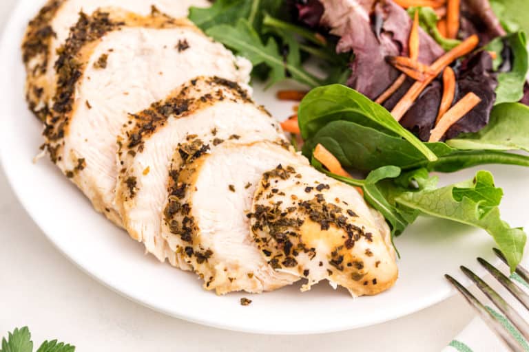 Sliced turkey tenderloin on a plate with green salad.