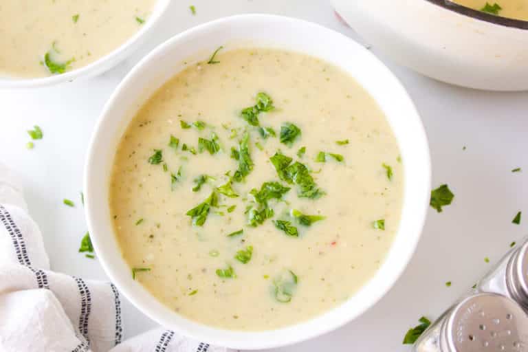 A small white bowl of zucchini potato soup garnished with parsley.