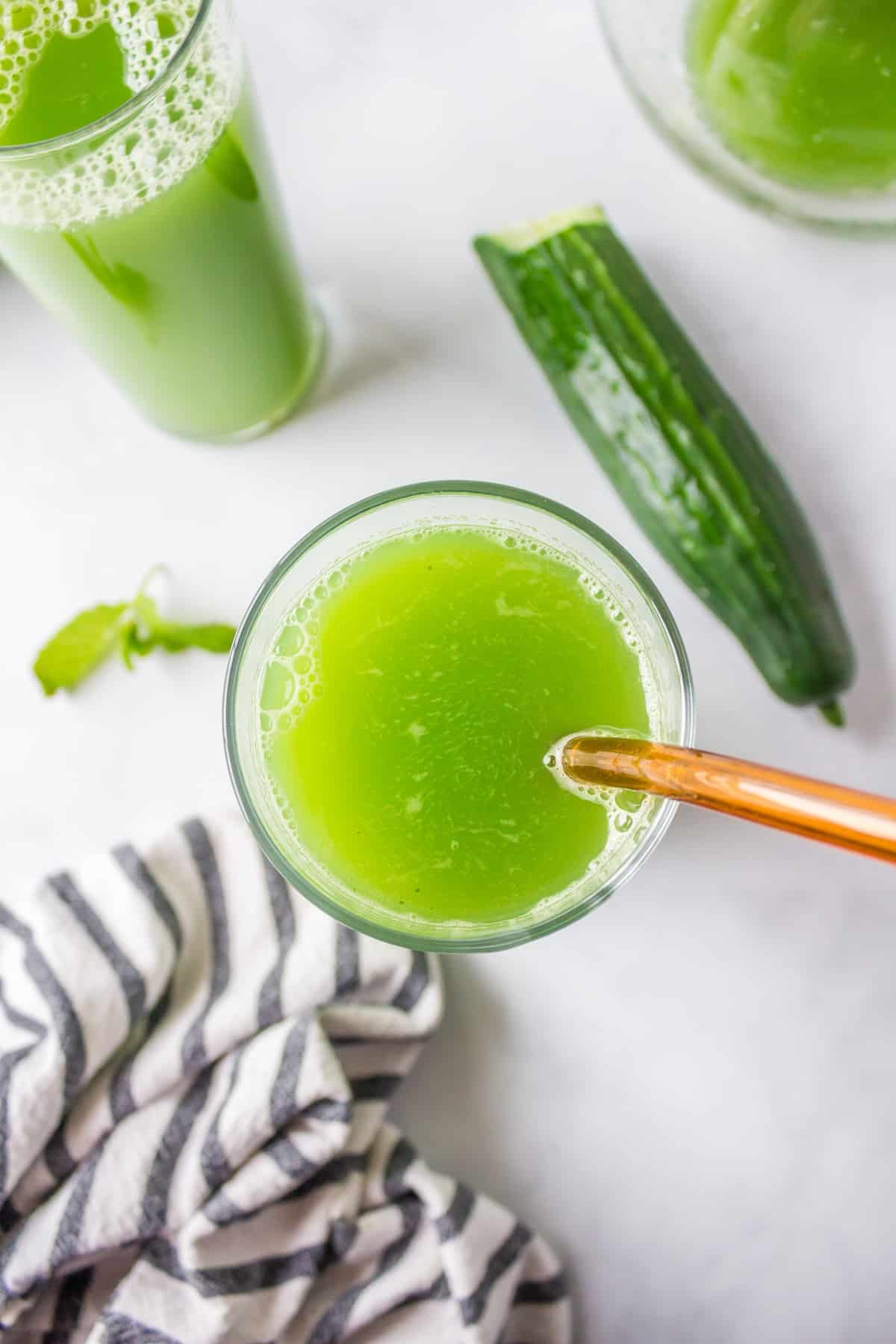 green cucumber juice in clear glass with straw.