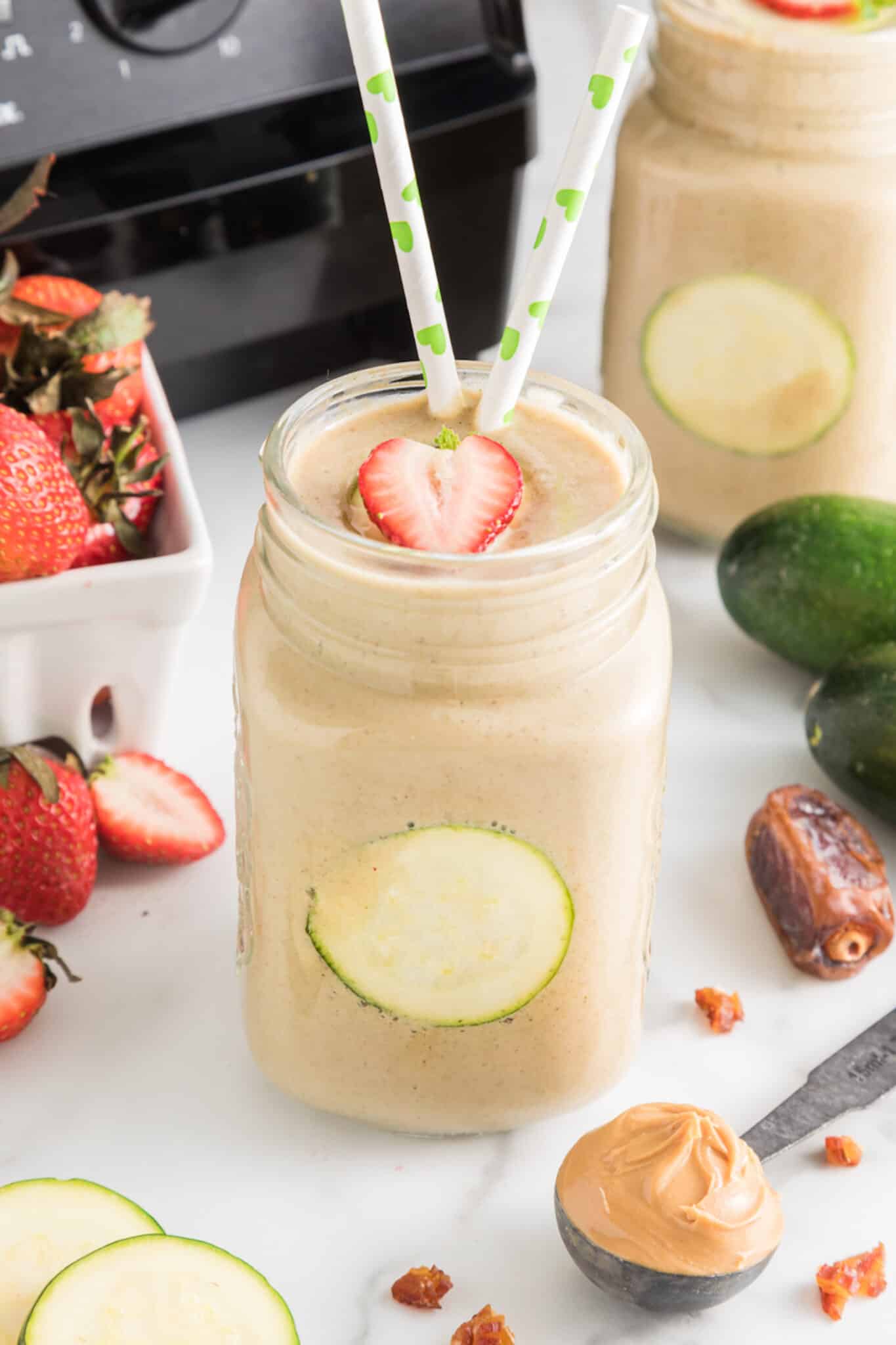Strawberry zucchini smoothie in a mason jar with two straws.