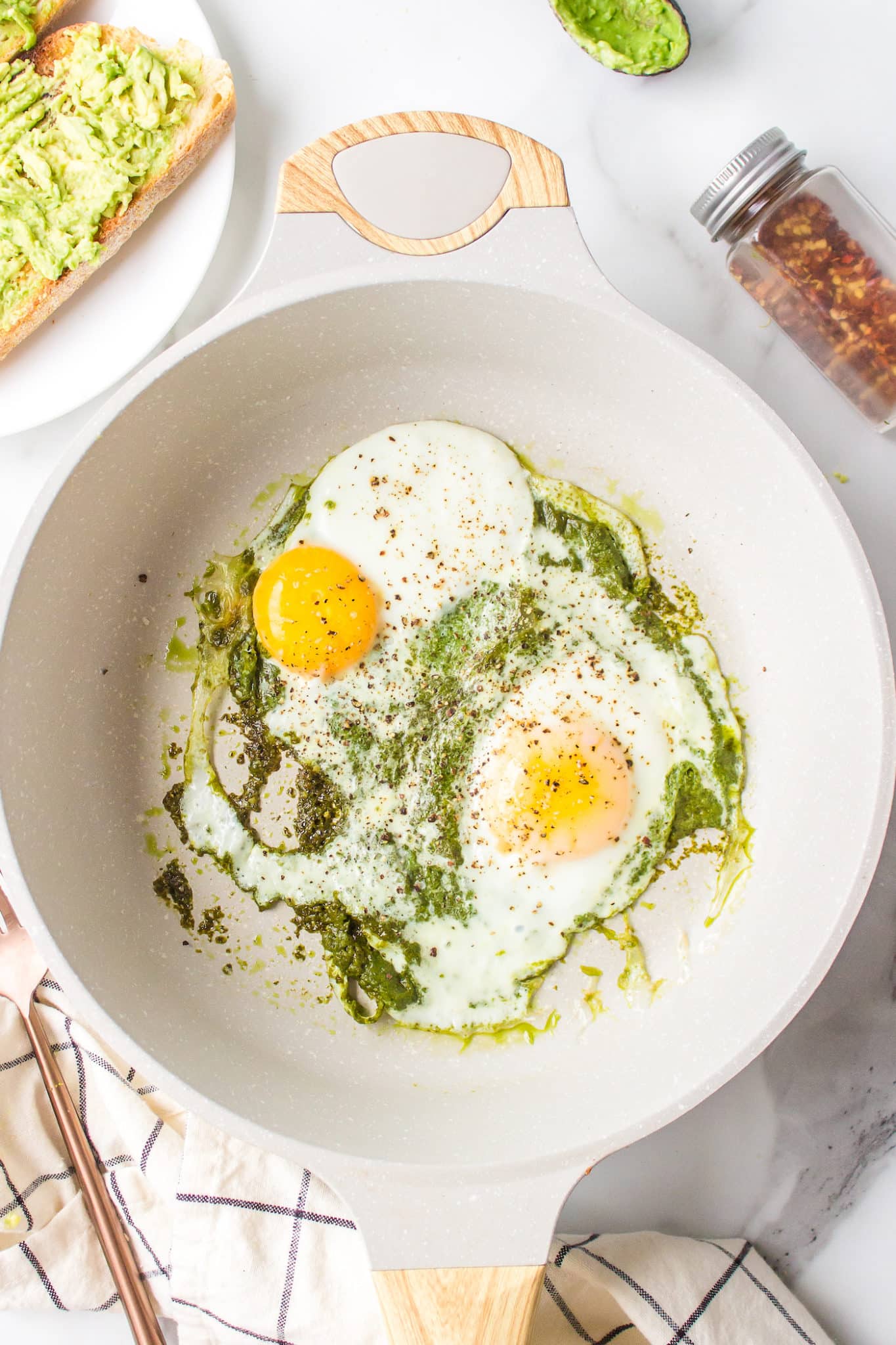 Two eggs in a skillet of warmed pesto.