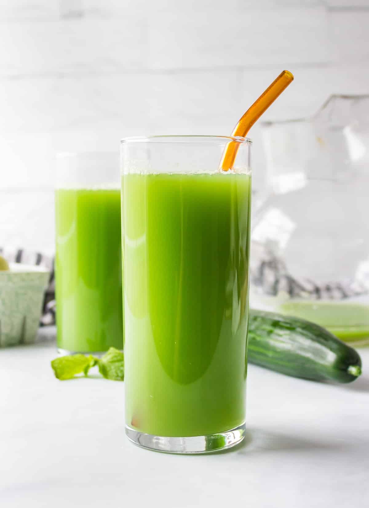 glass of pretty green juice on countertop with straw.