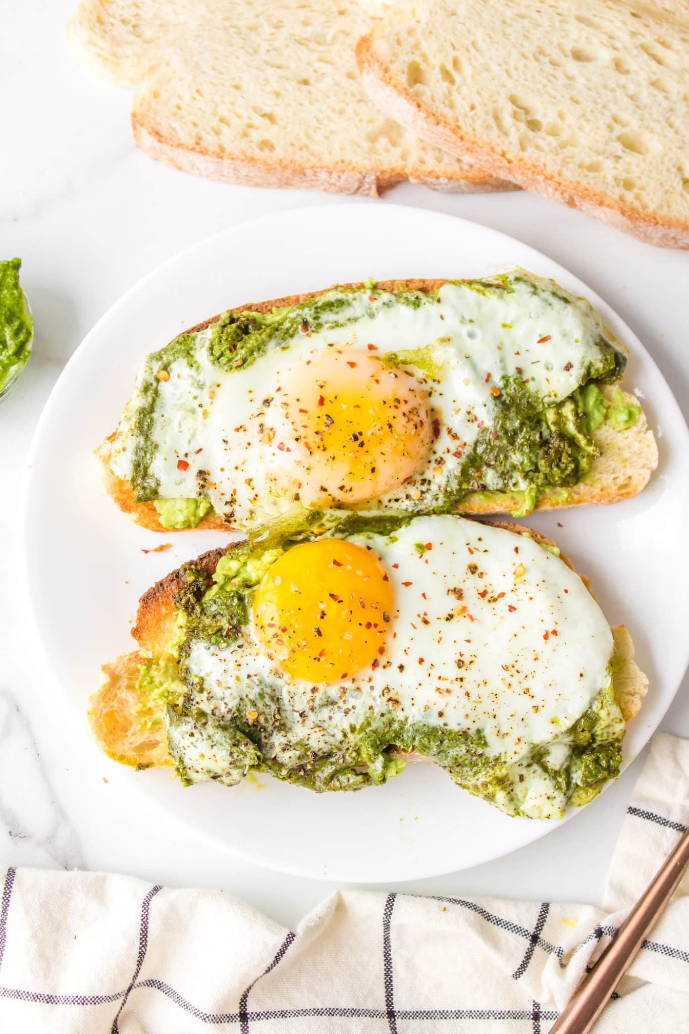Pesto fried eggs on slices of avocado toast on a white plate.