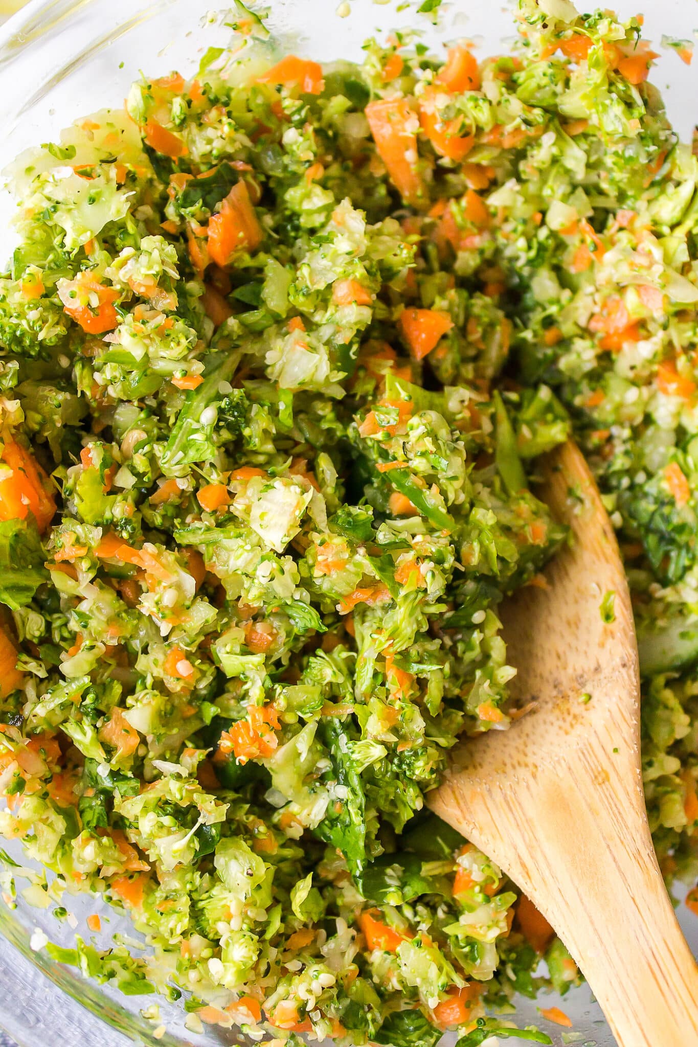 Chopped veggies salad in a glass bowl with a wooden spoon.