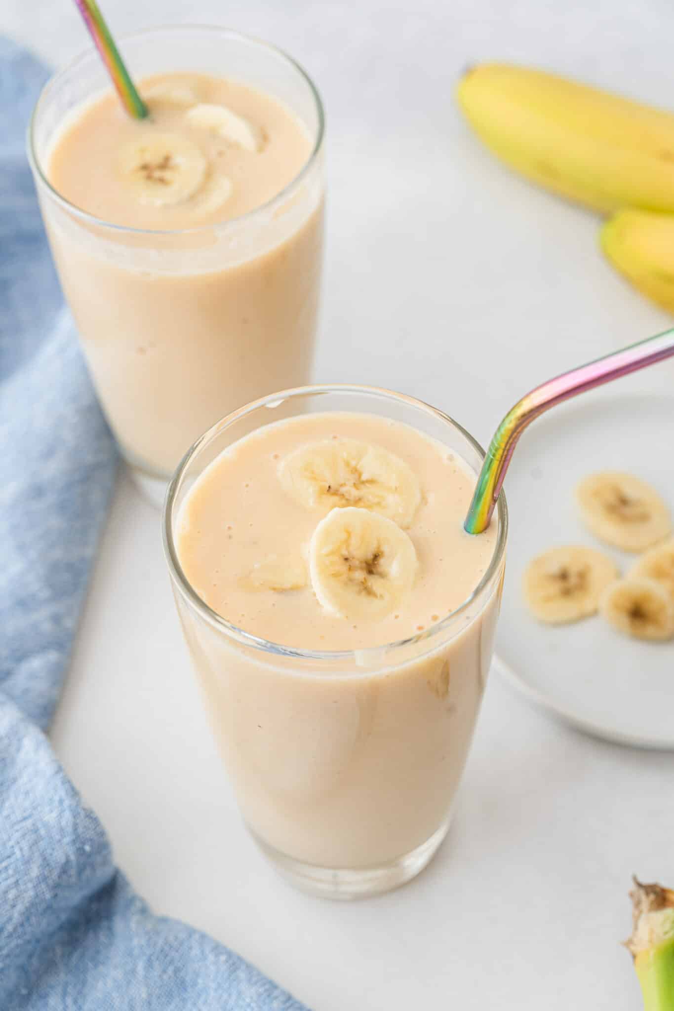 Banana peach smoothie in two glasses with iridescent straws.