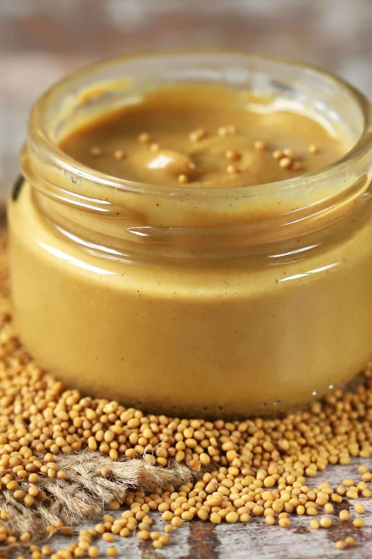 Jar of dijon mustard with scattered mustard seeds.