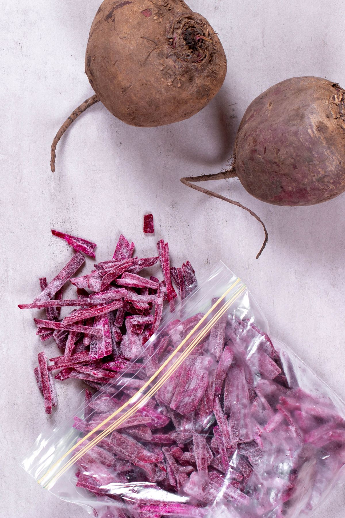 A baggie of frozen shredded beets next to two whole beets.