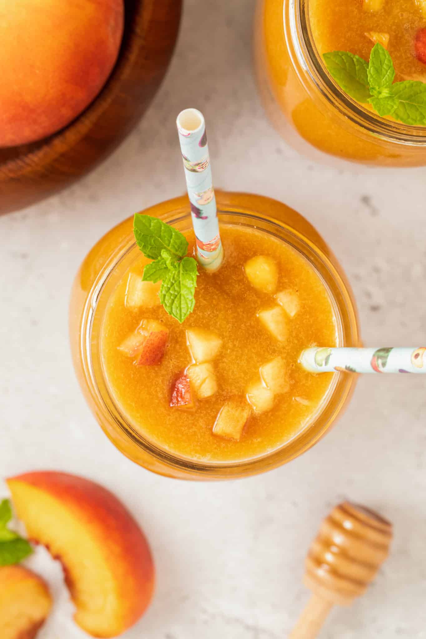 Top view of a jar of peach juice with two straws and peach chunks on top.