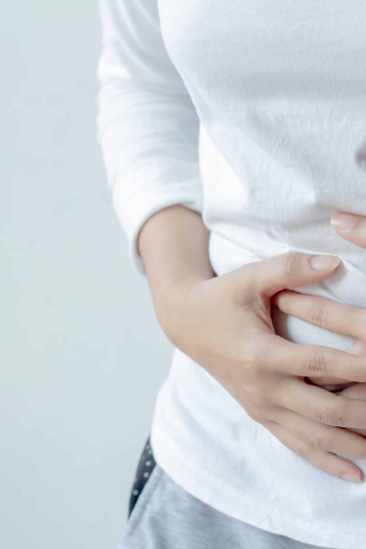 Woman in a white shirt holding stomach area with both hands.