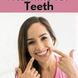 Brunette woman smiling and pointing to teeth with both index fingers.