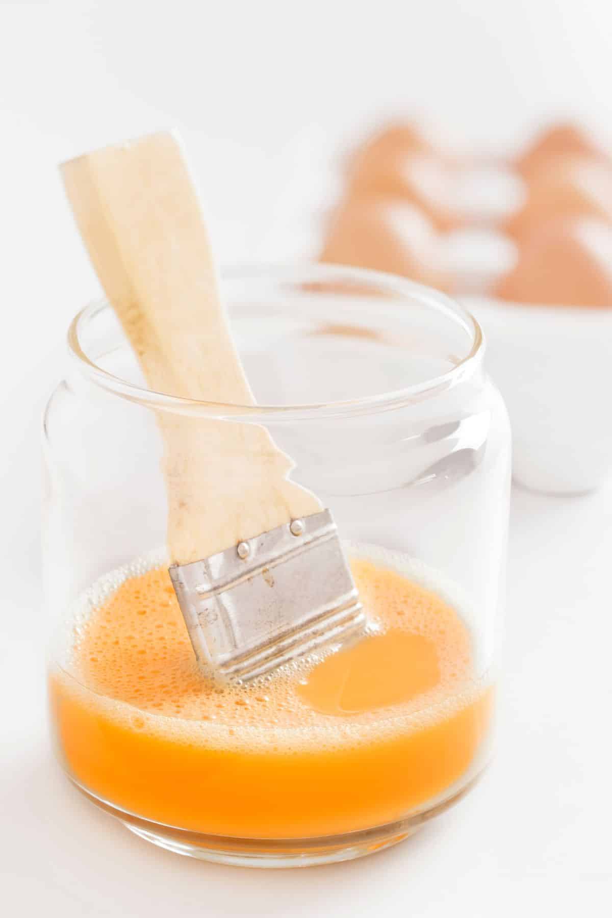 Clear glass of egg wash with brush.