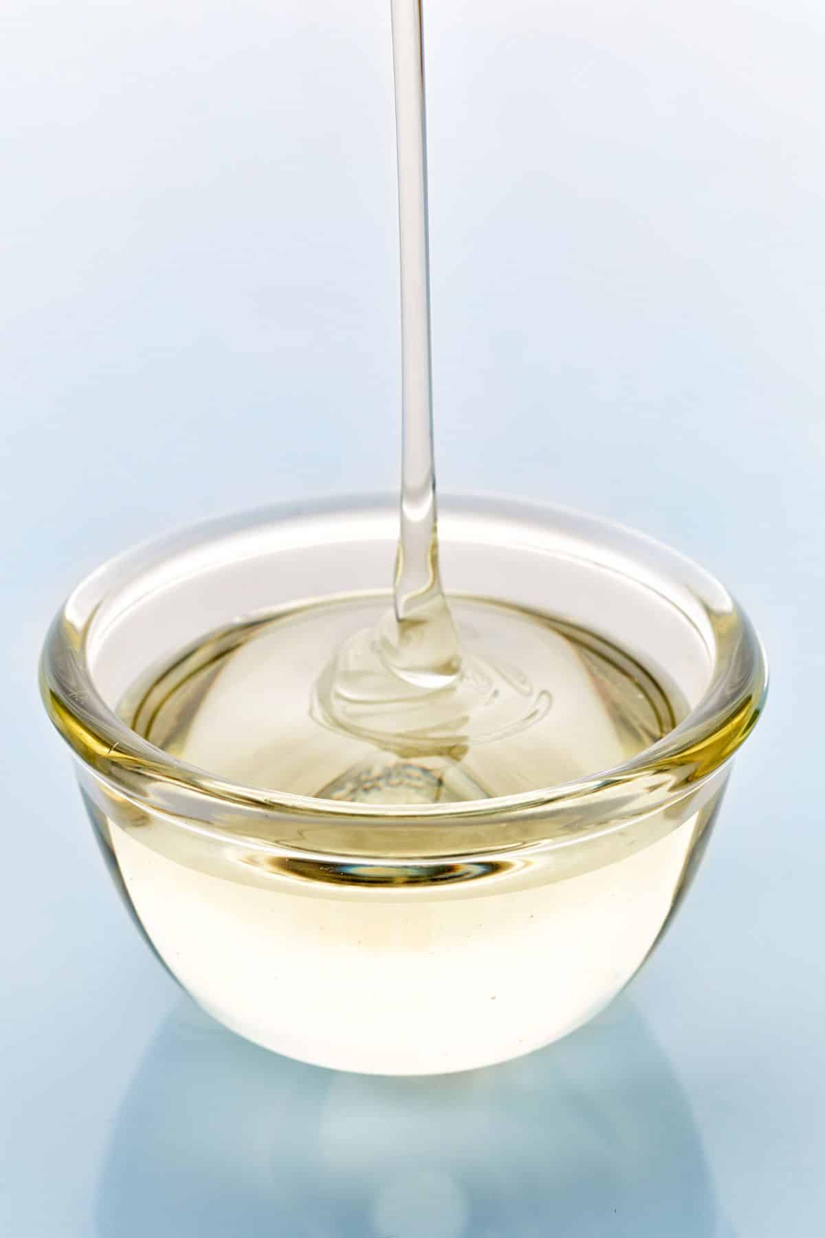 Light corn syrup pouring into clear bowl on light background.
