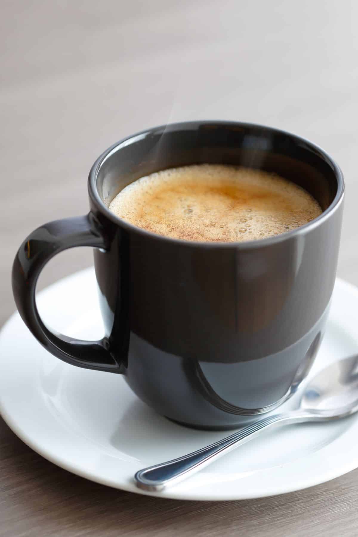 Frothy maca coffee in a black mug on a white saucer.