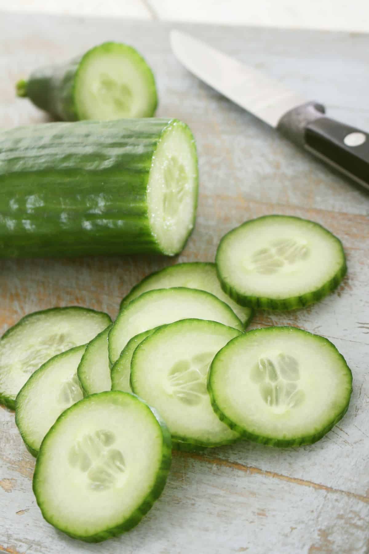 Halved and sliced cucumber on wooden surface.
