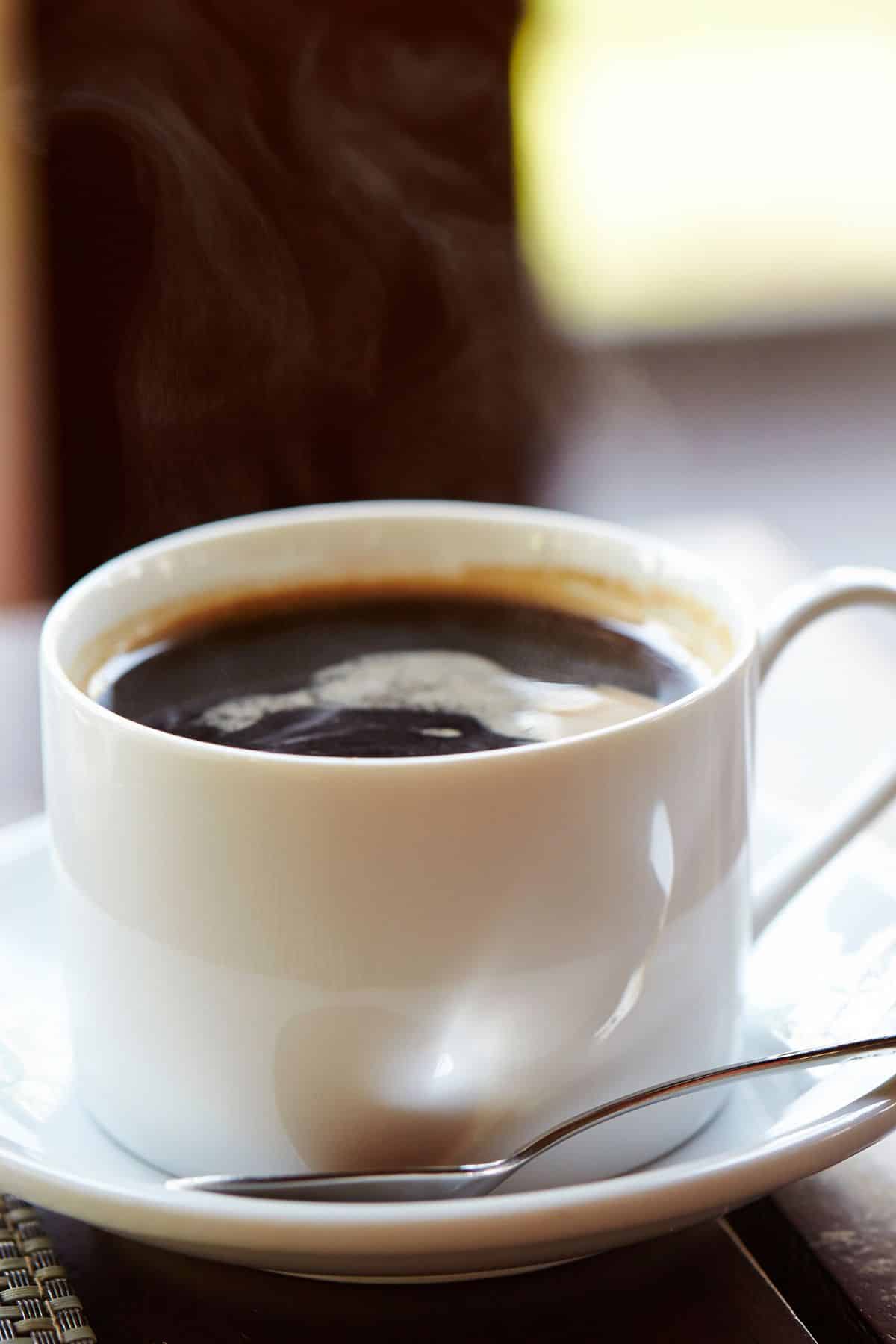 A small mug of maca coffee on a saucer with a spoon.