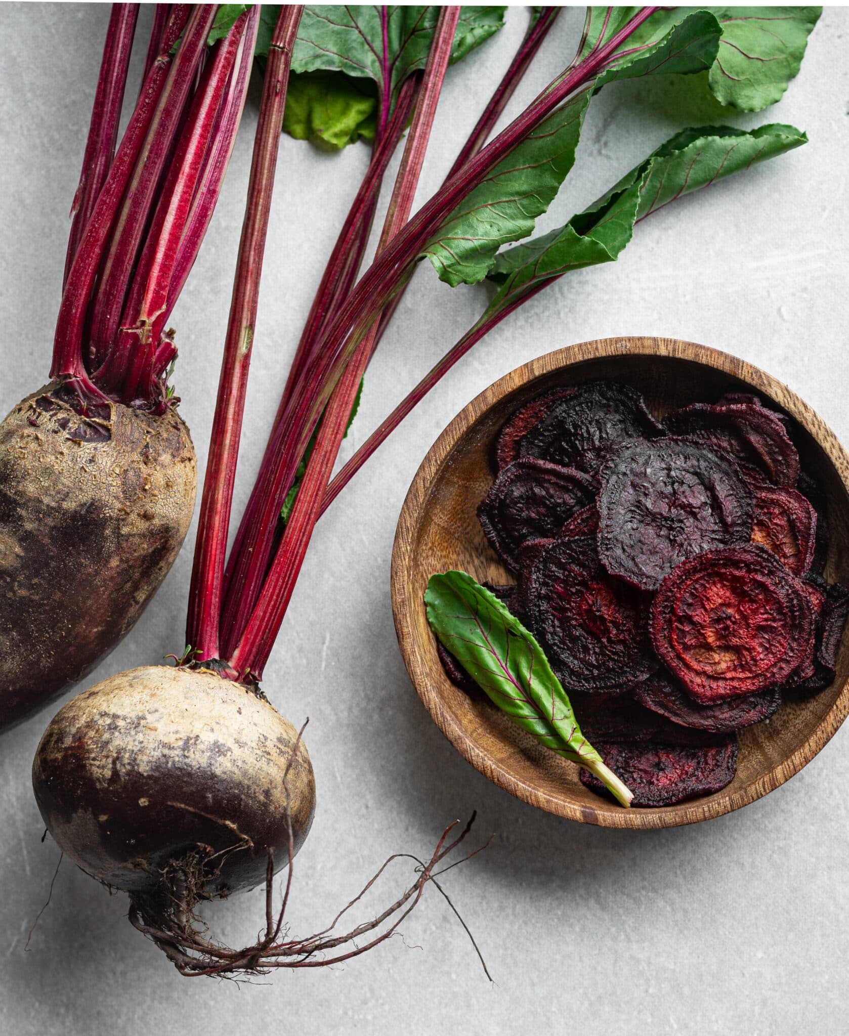 Dehydrated beet chips in a wooden bowl next to fresh beets.