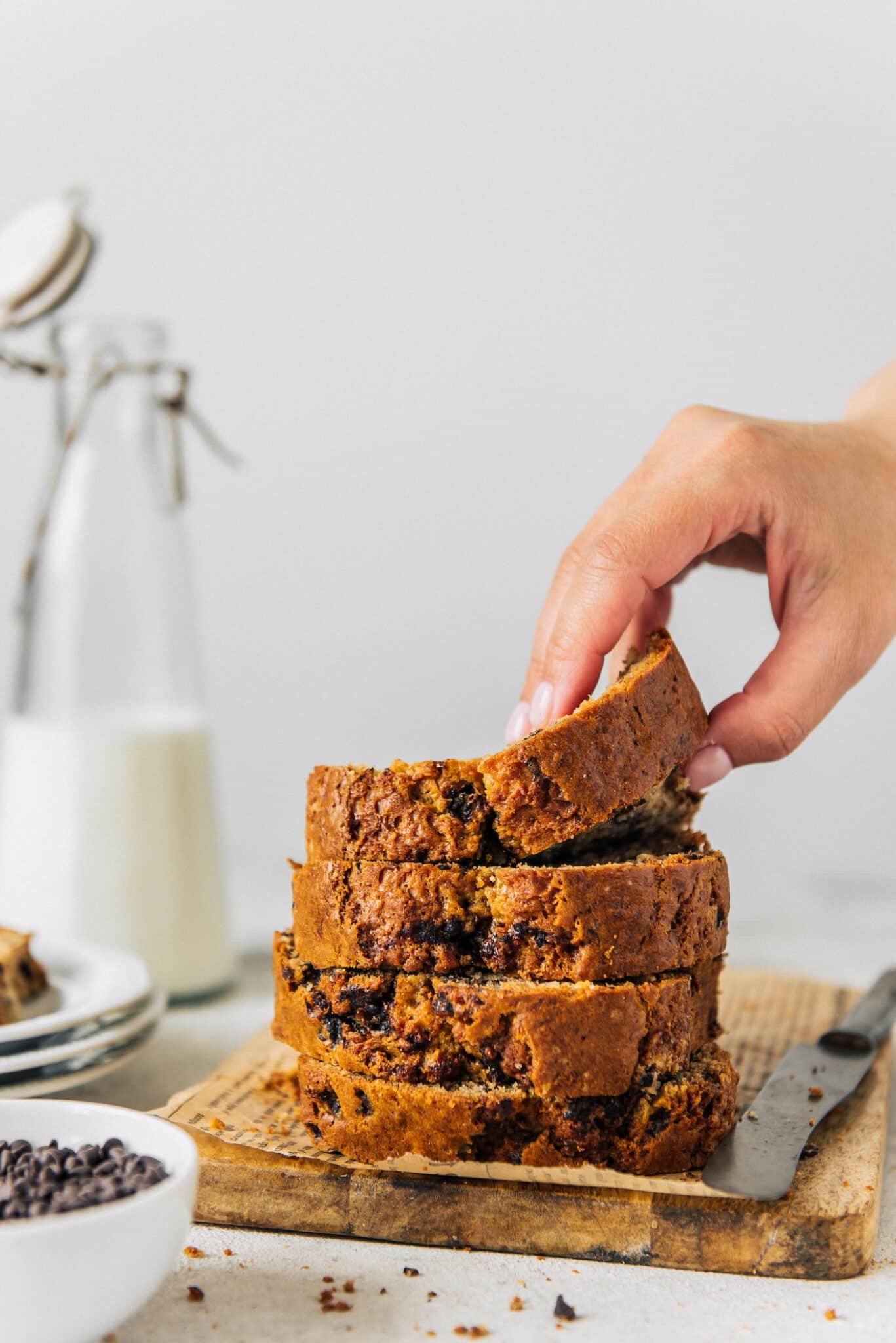 hand grabbing a thick slice of banana bread off of a table.
