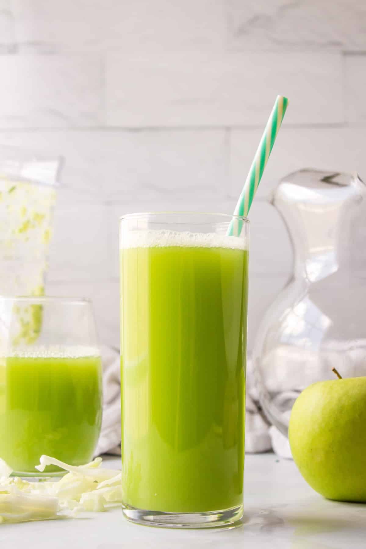 clear glass with green juice and a striped straw for serving.