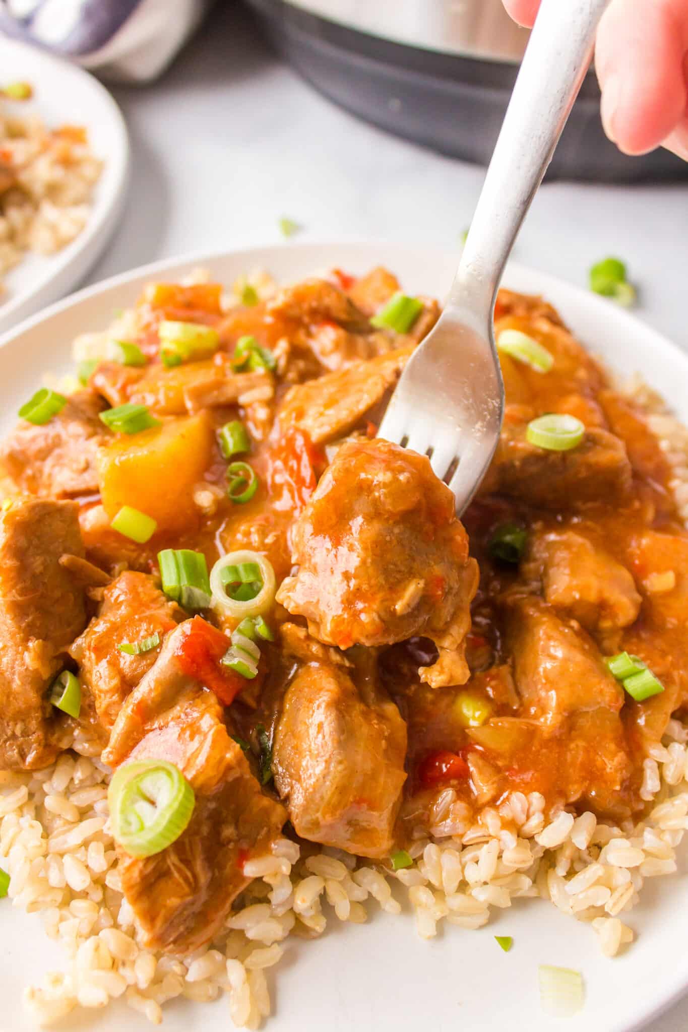 A fork with a bite of sweet and sour pork over a plate of brown rice.