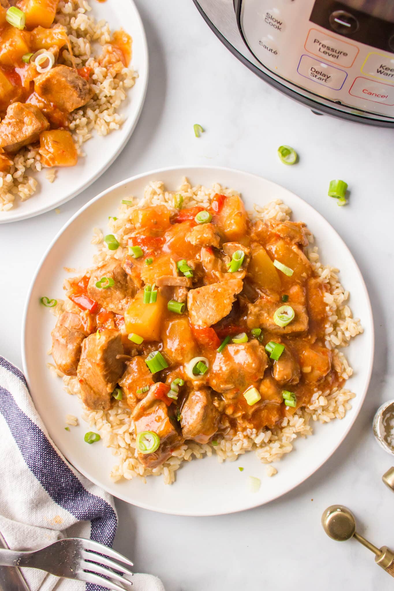 A white dinner plate of brown rice topped with sweet and sour pork.