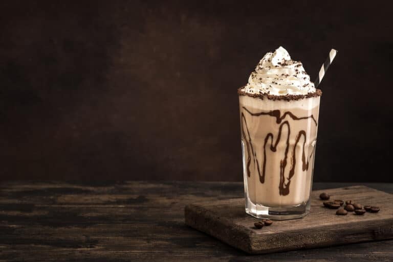 a dairy-free iced mocha topped with whipped cream in a glass with chocolate syrup.