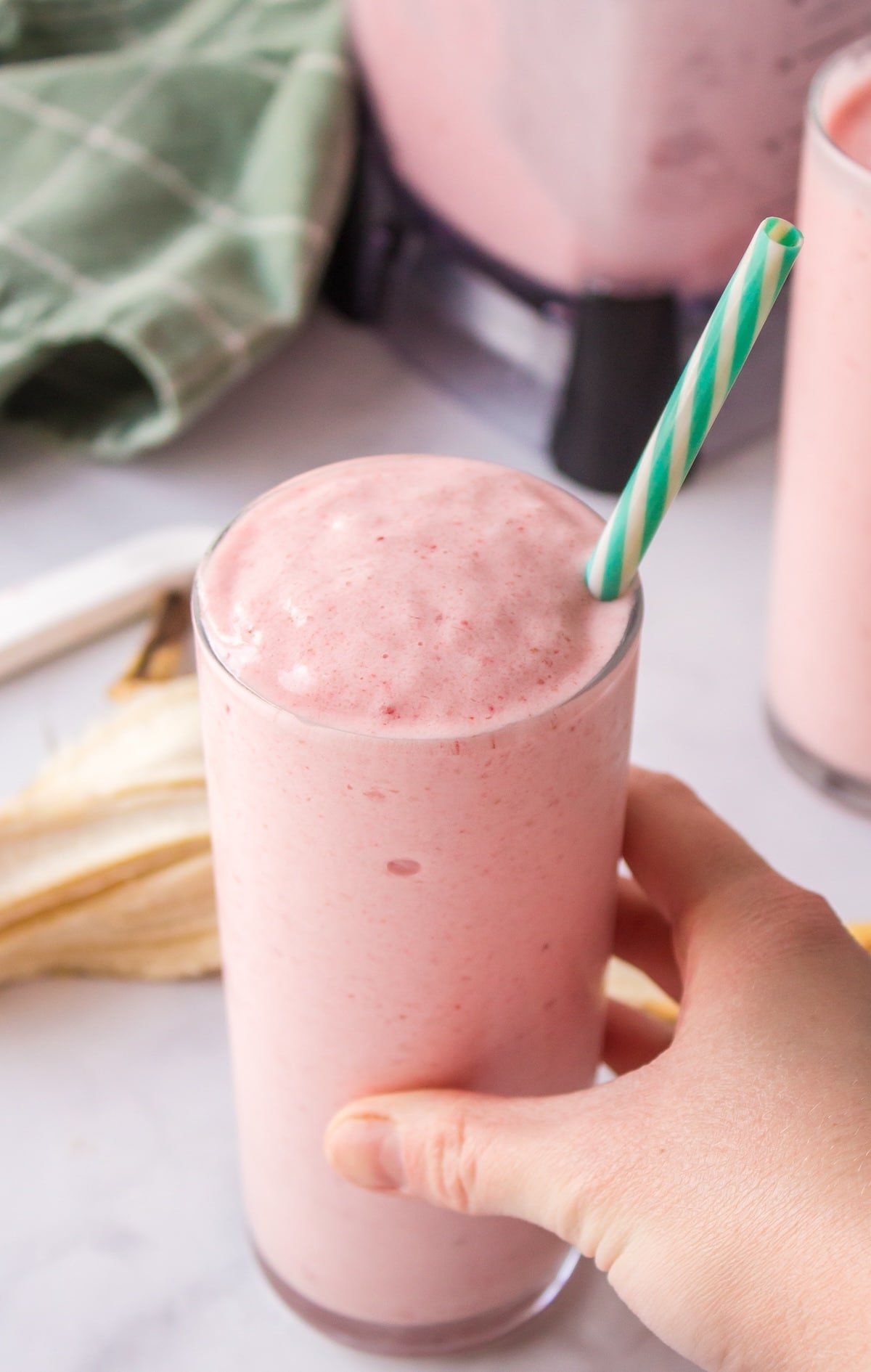 a person holding a glass of strawberry banana smoothie.